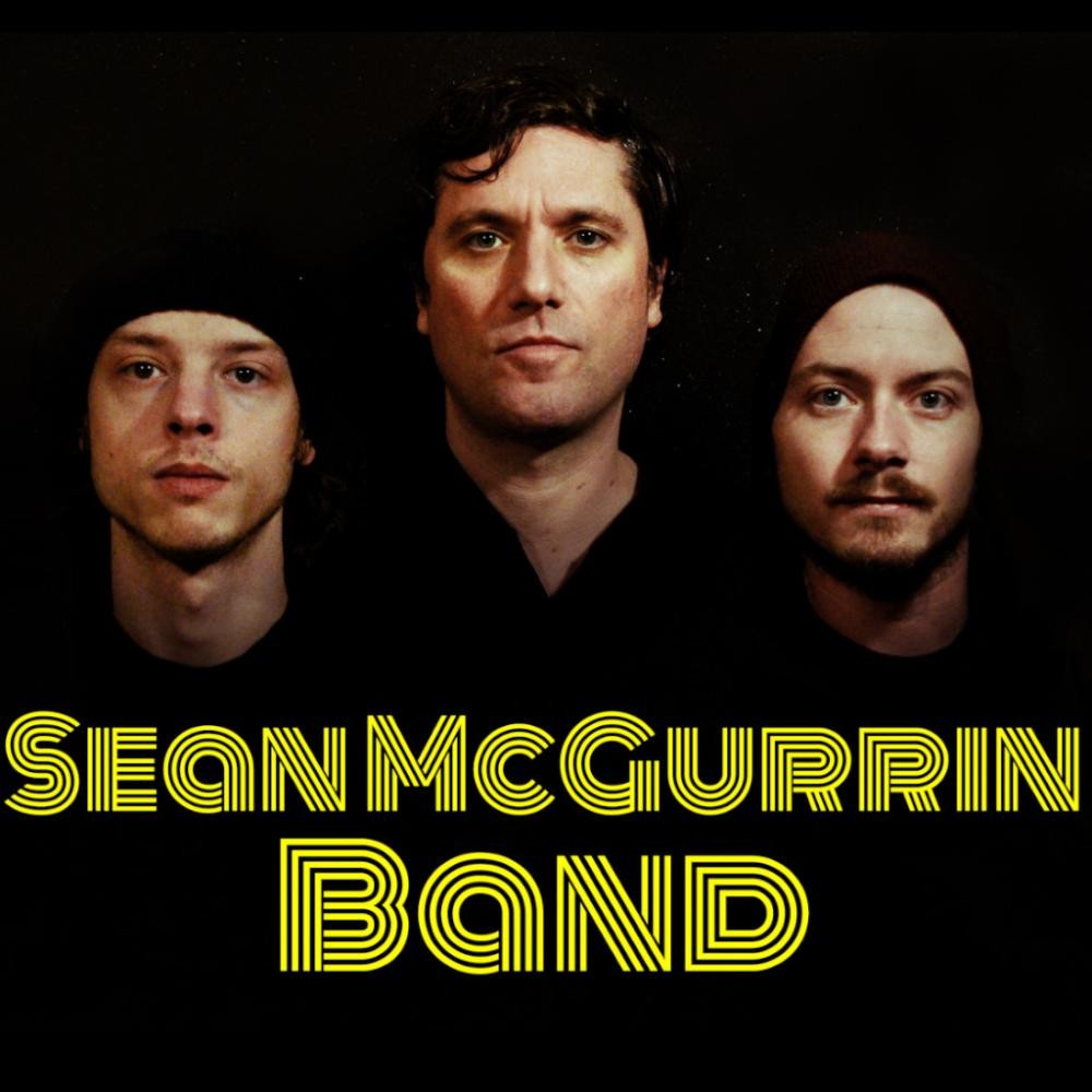 Die Köpfe der drei Mitglieder der Sean McGurrin Band vor schwarzem Hintergrund, darunter der Text SeanMcGurrin Band