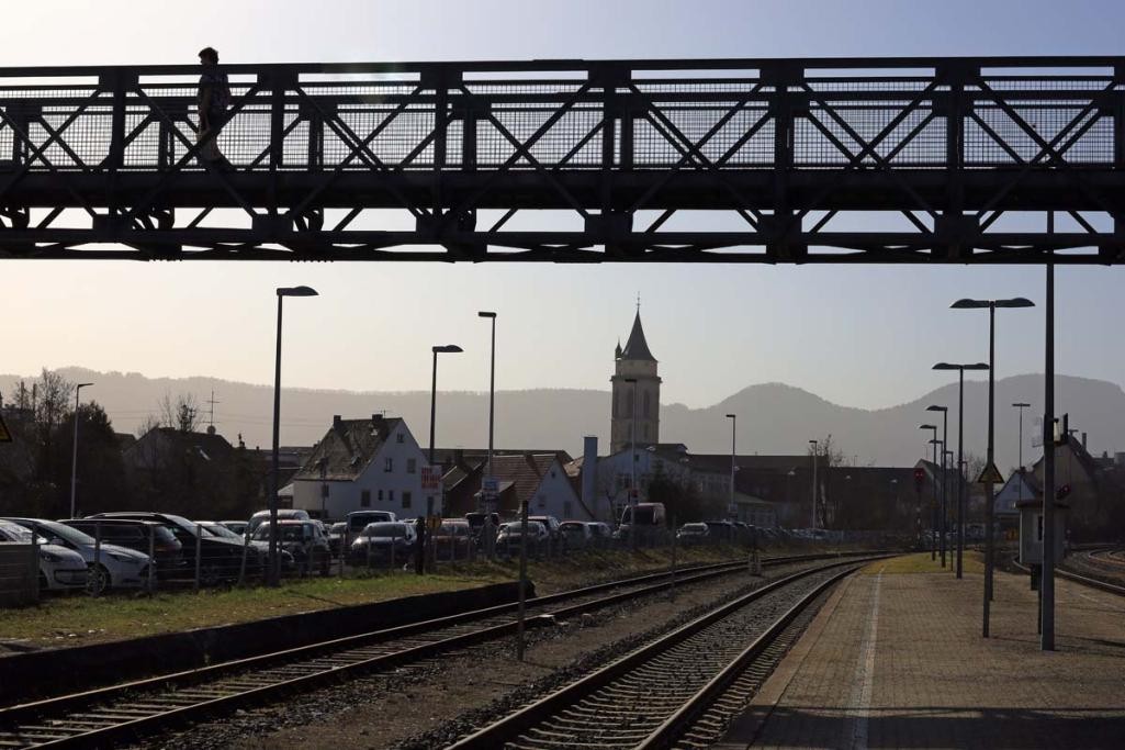 Blick über Schienen vom Balinger Bahnhof in Richtung Stadtkirche, links Parkplatz, oben Fußgängerbrücke