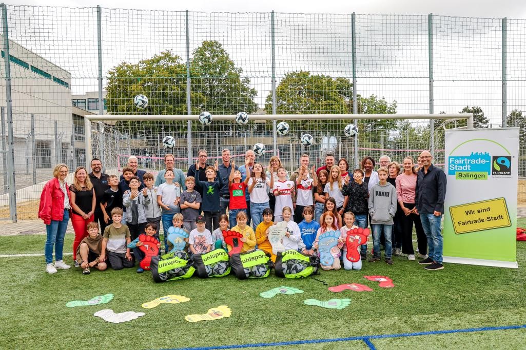 Lehrer und Kinder stehen vor einem Fußballtor und werfen die Fairtrade Fußbälle hoch