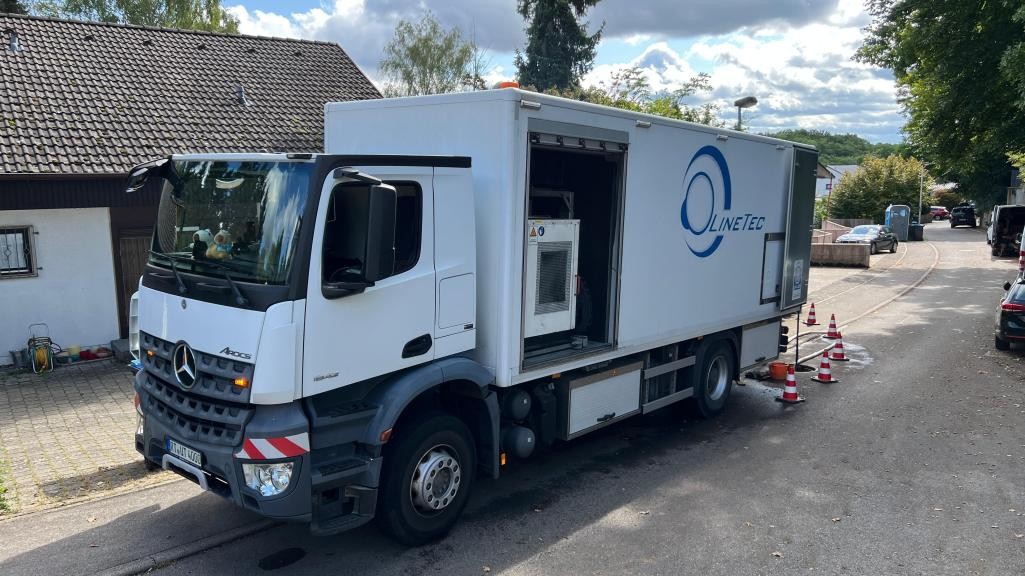 Ein Lastwagen auf einer Straße vor einem Haus mit abgesperrtem Kanaldeckel