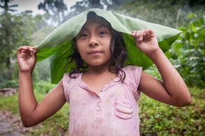 Ein Mädchen schützt sich mit einem Bananenblatt vor dem Regen