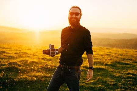 Thomas B. Jones hält eine Kamera in der Hand und posiert vor dem Sonnenuntergang 
