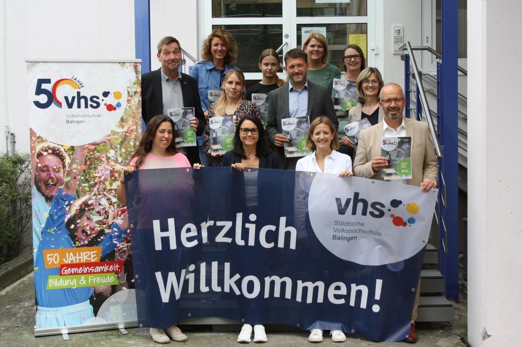 Eine Gruppe Personen mit einem Banner der Volkshochschule auf den Treppen vor dem Gebäude