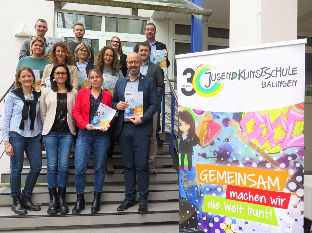 Mehrere Personen verschiedenen Geschlechts stehen auf einer Treppe und präsentieren das neue VHS-Programm