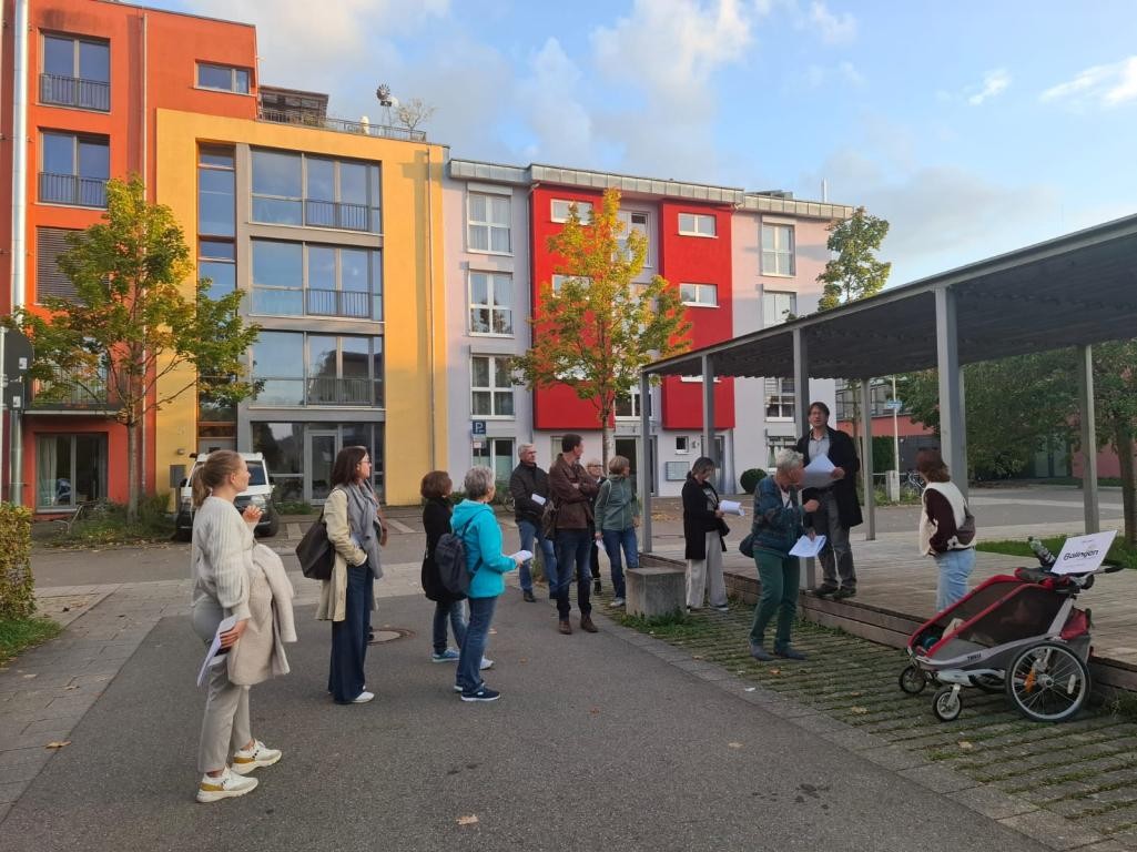 Eine Gruppe von Menschen in herbstlicher Kleidung vor einem bunten Gebäude