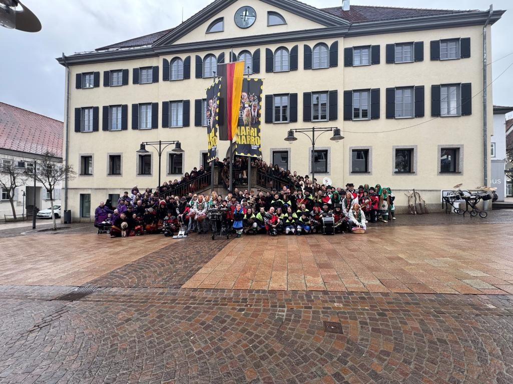 Das Rathaus mit einer großen Gruppe verkleideter Menschen vor der Freitreppe, am Fahnenmast eine Deutschlandfahne gerahmt von zwei Fasnetsflaggen