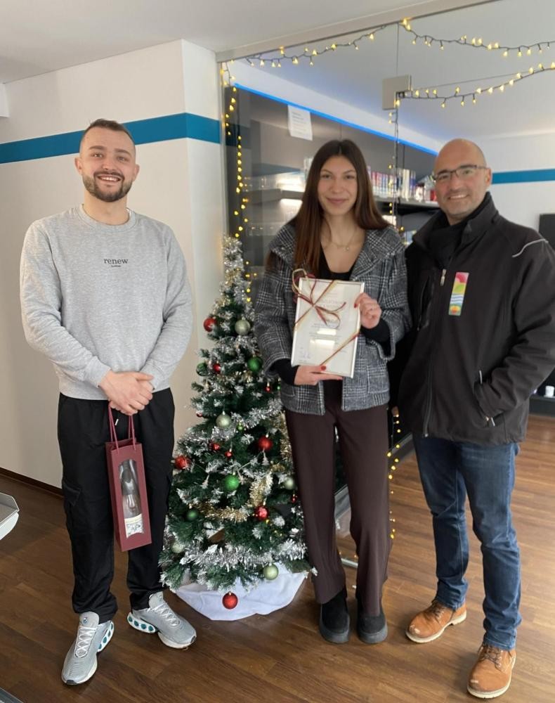 Zwer Männer und eine Frau stehen im Kioskladen vor einem kleinen geschmückten Baum 