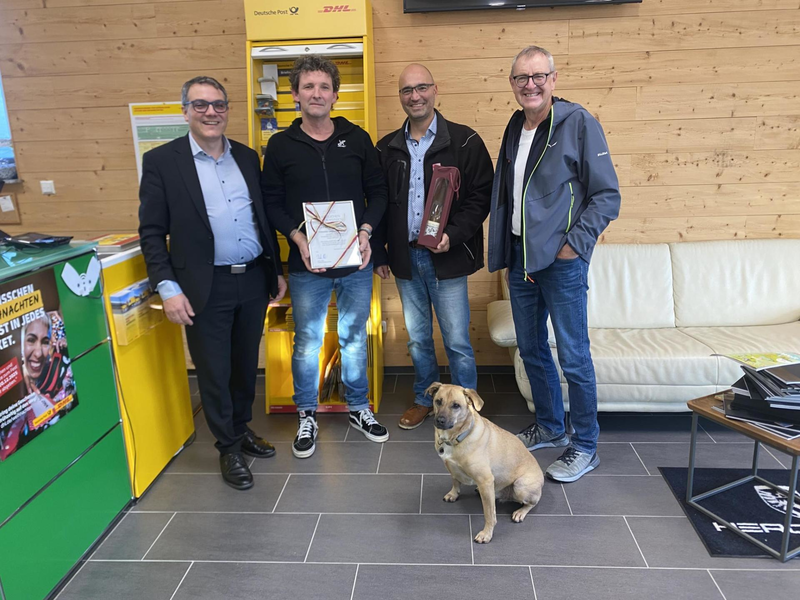 Drei Männer und ein Hund stehen im Ladengeschäft und freuen sich über die Eröffnunge der neuen Postfilalie