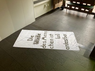 Werk "Die Würde des Menschen" Eine weiße Fahne mit einem Schriftzug liegt auf dem Boden