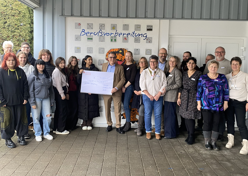 Menschen stehen vor der Wand mit einem Spendenscheck in der Hand