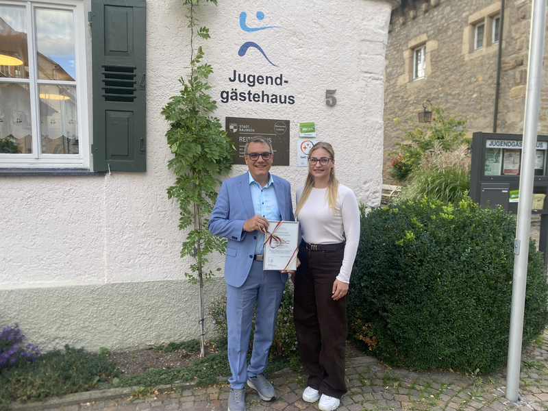 Mann und Frau stehen mit der Urkunde vor dem Jugendgästehaus Mann und Frau stehen mit der Urkunde vor dem Jugendgästehaus